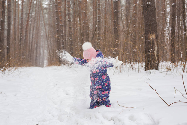 Childhood and people concept - child girl walking in the winter outdoors and throwing the snow up - Photo, Image