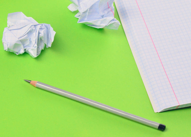 Notebook with pencil and white crumpled paper ball on green background. Concept of no idea, education, minimalism - 写真・画像