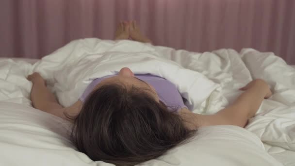 Beautiful teen girl wakes up in bed and smiles stock footage video - Záběry, video