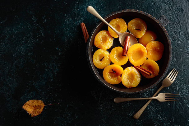 Peach dessert with cinnamon and cloves on a dark background, top view. - Photo, Image