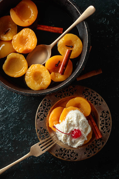 Peach dessert with cinnamon, cream and cherry on a dark background, top view. - Photo, Image