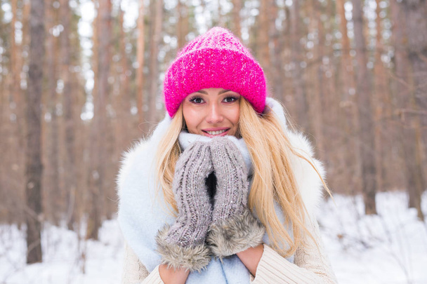 Beauty, winter and people concept - Attractive blonde woman in a pink sweater in the snowy forest is smiling - Photo, Image