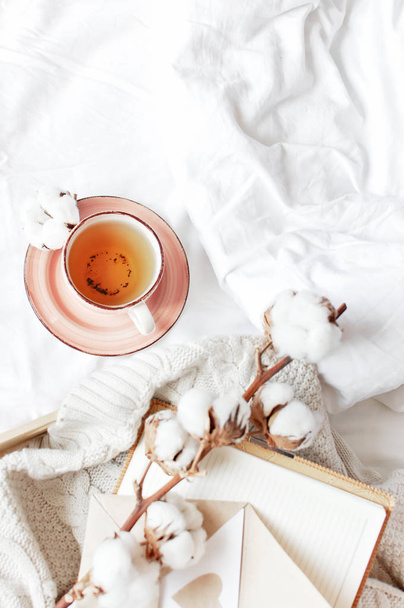 Cup of hot tea branch of cotton wooden tray knitted plaid sweater open notebook love letter in bed. Cozy morning breakfast at home Lifestyle gentle background Copy Space autumn winter concept - Photo, Image