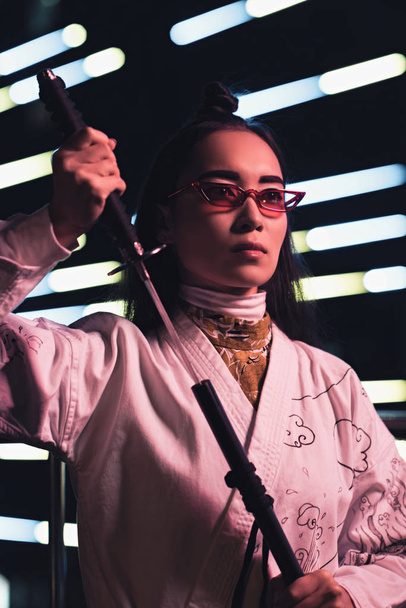attraktive asiatische Mädchen im weißen Kimono unter Katana auf der Straße mit Neonlicht am Abend, Stadt der Zukunft Konzept - Foto, Bild