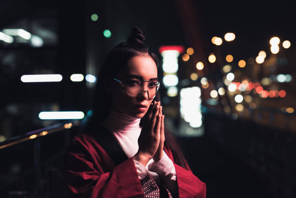 gyönyörű ázsiai lány bordó kimonó így namaste gesztus utcában este, a jövő koncepció város neon fénnyel - Fotó, kép