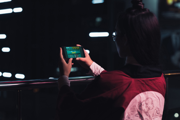 Widok z dziewczynka trzymając smartfon z sportowe bet urządzenia na ulicy z neon światło wieczorem, miasto przyszłości koncepcja tyłu - Zdjęcie, obraz