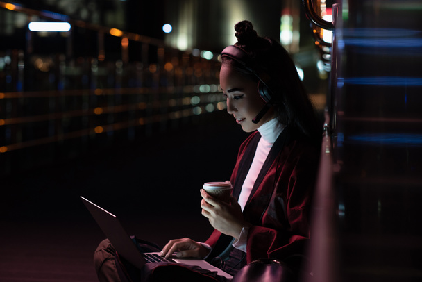 привлекательная азиатская девушка в кимоно сидя и видео-чат на улице с неоновым светом, город будущей концепции
 - Фото, изображение