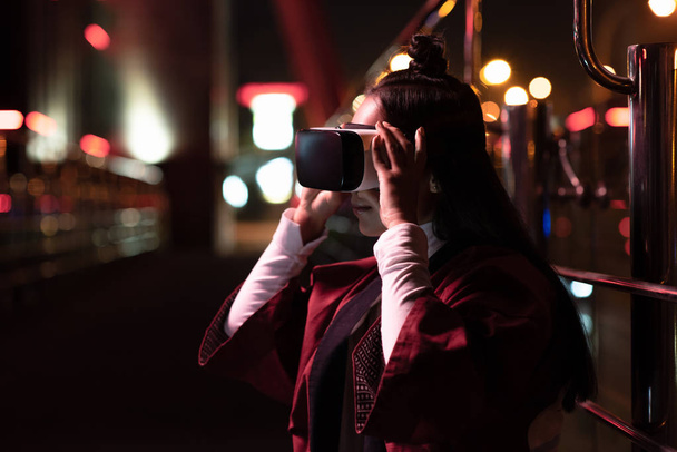 atraktivní asijské dívka pomocí soupravu pro virtuální realitu na ulici v večer, město budoucí koncepce - Fotografie, Obrázek