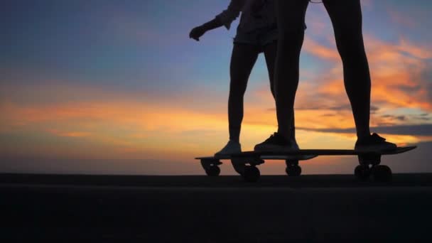 Gros plan sur les jambes de deux filles petite amie en short et baskets monter planches à roulettes sur la pente contre le beau ciel du soleil levant. Ralenti 120 ips
 - Séquence, vidéo