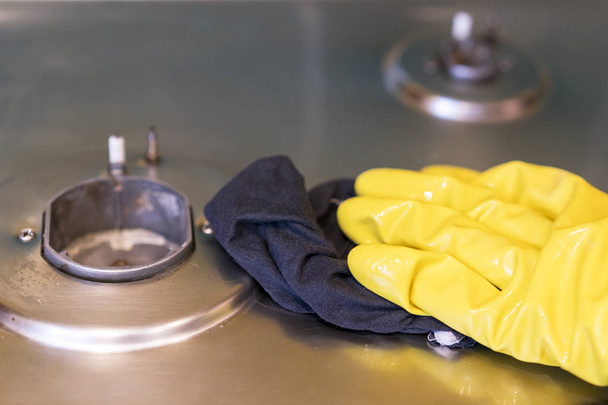 Μια γυναίκα στα προστατευτικά γάντια πλένει το φυσικό αέριο σόμπα. - Φωτογραφία, εικόνα