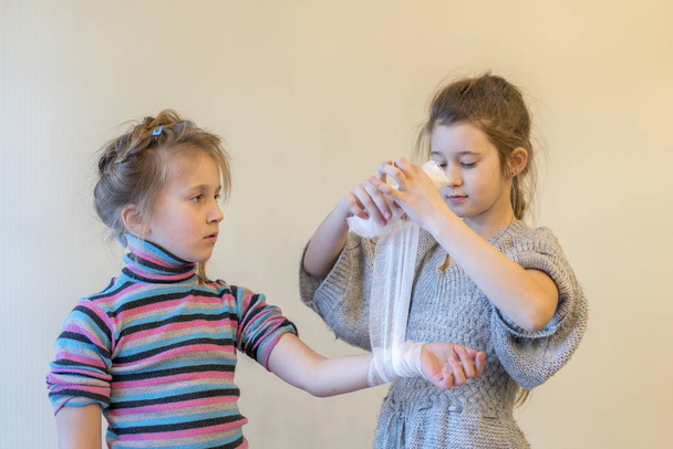 少女は、彼女の妹の手を曲げします。2、女の子、再生、医師。包帯で腕を包帯します。手の外傷最初の援助. - 写真・画像