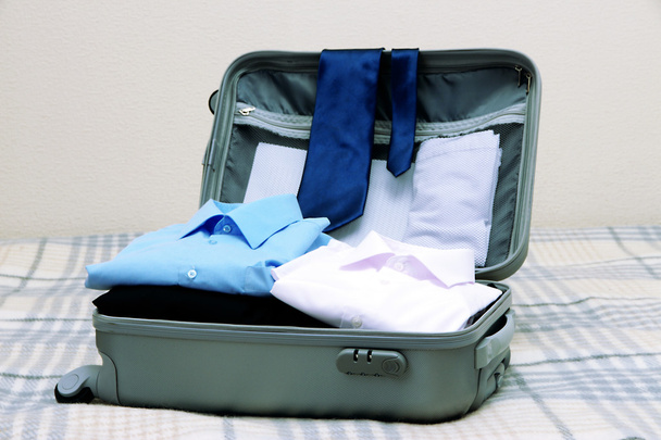 Open grey suitcase with clothing on bed - Valokuva, kuva