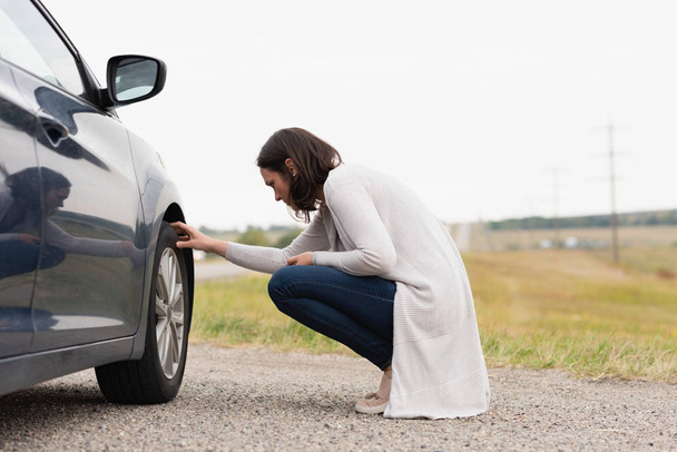 Вид сбоку женщины, проверяющей шину автомобиля во время поломки
 - Фото, изображение