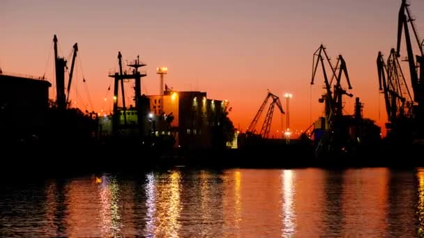 De haven van de zee bij zonsondergang van de dag. Prachtige rode zonsondergang op de achtergrond van portaalkranen. - Video