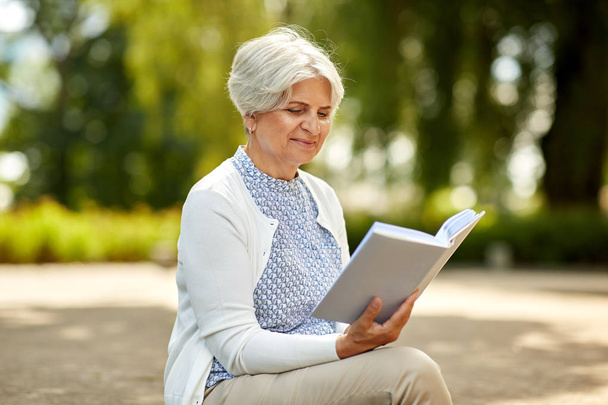 senior woman reading book at summer park - Foto, afbeelding
