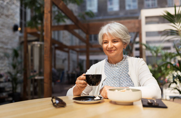mujer mayor bebiendo café en la cafetería de la calle
 - Foto, Imagen