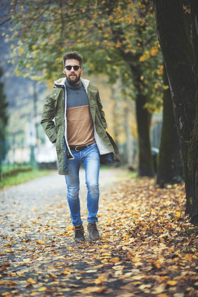 Casual hippie style man walking among autumn leaves. - 写真・画像