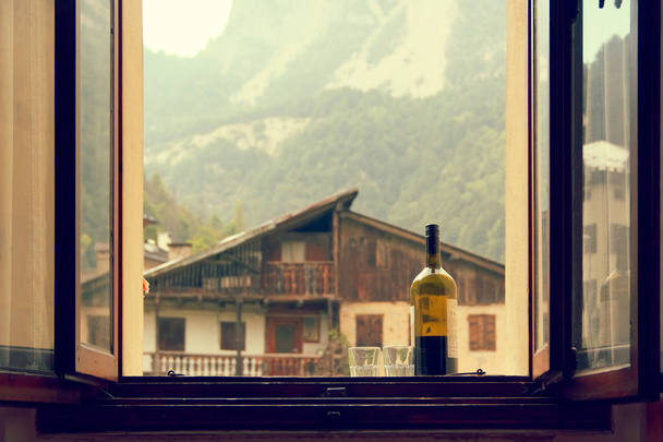 una botella de vino y 2 vasos en el alféizar de la ventana abierta
 - Foto, Imagen