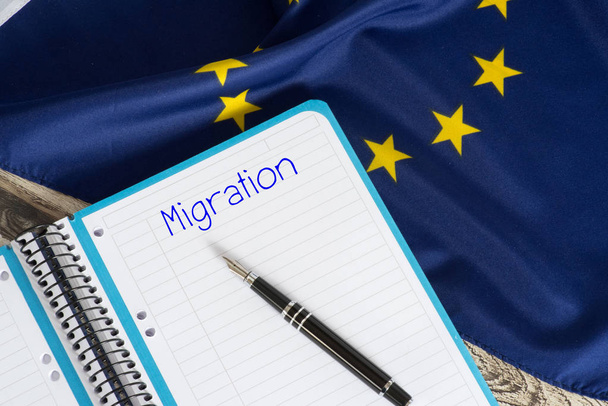 Σημαία της Ευρωπαϊκής Ένωσης ΕΕ και μια γραφή pad με τη λέξη μετανάστευση - Φωτογραφία, εικόνα