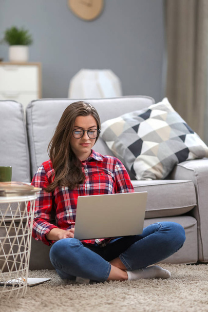 Porträt einer lächelnden Frau mit Brille am Laptop, während sie es sich zu Hause auf der Couch gemütlich macht. - Foto, Bild
