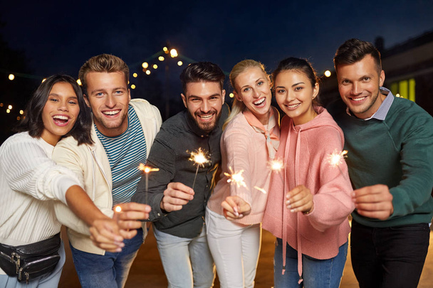happy friends with sparklers at rooftop party - 写真・画像