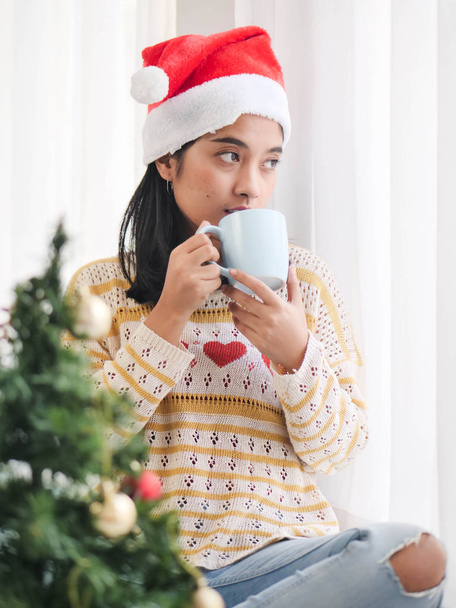 Asian woman wearing santa hat and holding coffee cup and look out window, lifestyle concept. - Foto, imagen