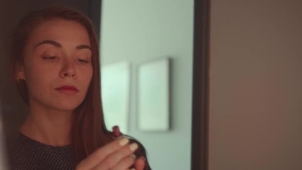 Gyönyörű vörös hajú lány elegáns ruha néz a tükörbe, és alkalmaz ajakrúzs-ra ajka előtt fél - video-ban lassú mozgás - Felvétel, videó