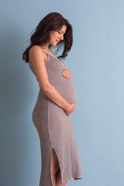 Portrait of happy pregnant woman with hands on belly isolated over blue background - Fotó, kép