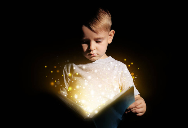 Petit garçon mignon lisant un livre magique sur fond sombre
 - Photo, image