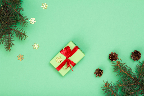 Weihnachtsdekoration. Geschenkkarton, Tannenzweige mit Zapfen und dekorativen Schneeflocken auf grünem Hintergrund. Ansicht von oben. Weihnachtsgrußkarten-Konzept. - Foto, Bild