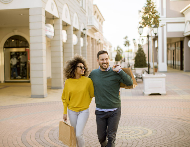 Nuori ja iloinen pari kävelee pitkin katua ostoskassien kanssa
 - Valokuva, kuva