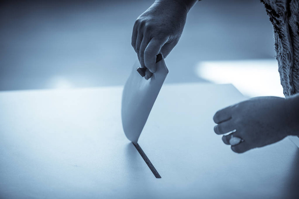 Color image of a person casting a ballot at a polling station, during elections. - 写真・画像