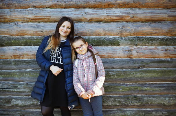 Portrait of mother with daughter against the background of an old wooden log wall. Space for text. - Foto, immagini