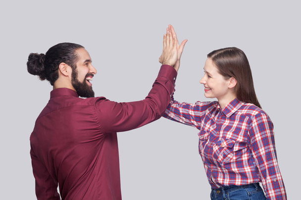 Portrait of happy satisfied bearded man and woman in casual style celebrating triumph together while giving hi five hands on gray background - Foto, imagen