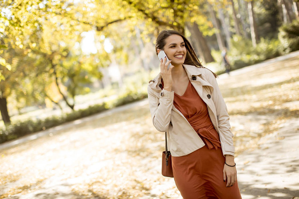 Gelukkig jonge vrouw met behulp van mobiele telefoon in de herfst park op mooie dag - Foto, afbeelding