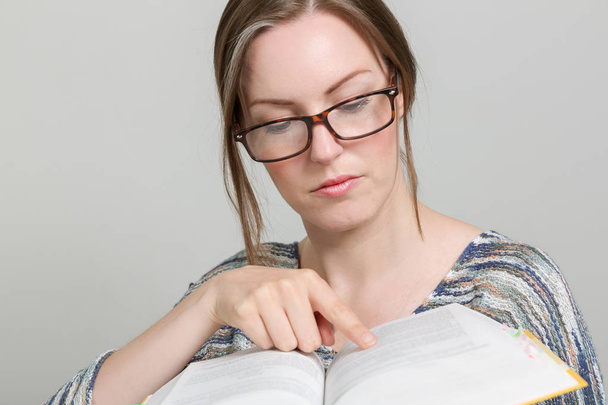 jeune femme avec des lunettes est à la recherche dans un livre
 - Photo, image