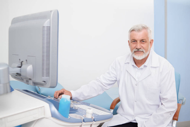 Senior man sitting at ultrasound apparatus at hospital. - Fotó, kép