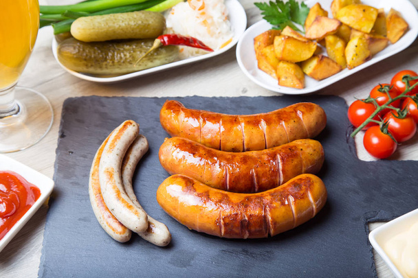 Grilled sausages with potatoes, cucumbers and sauerkraut, with two sauces. Close-up, selective focus. - Photo, image