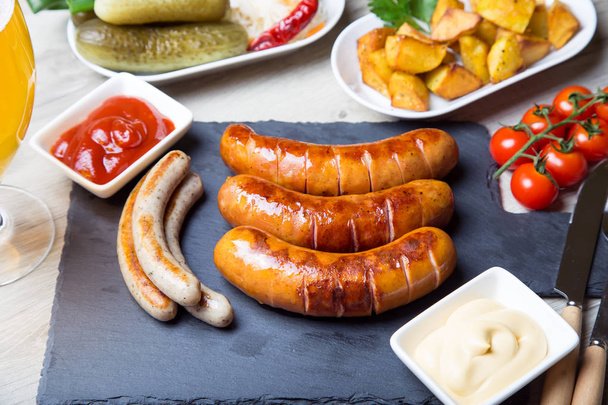 Grilled sausages with potatoes, cucumbers and sauerkraut, with two sauces. Close-up, selective focus. - Foto, Imagen