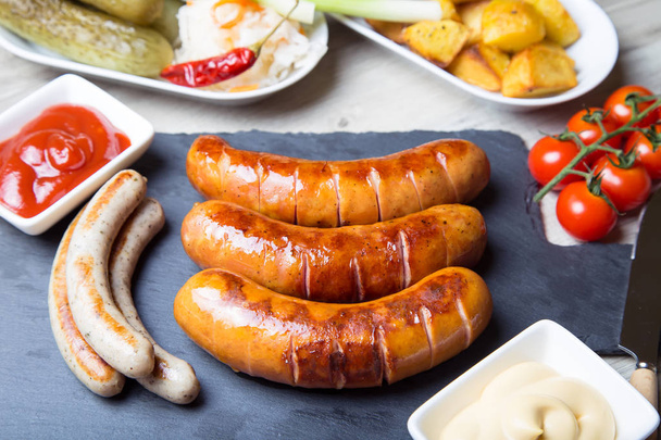Grilled sausages with potatoes, cucumbers and sauerkraut, with two sauces. Close-up, selective focus. - Foto, Bild