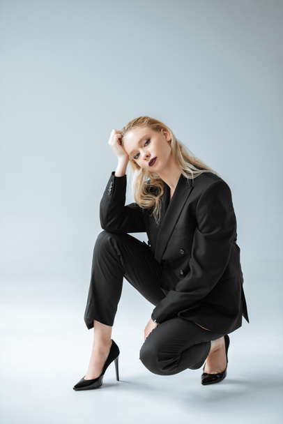 fashionable blonde model posing in trendy black suit on grey - Fotoğraf, Görsel