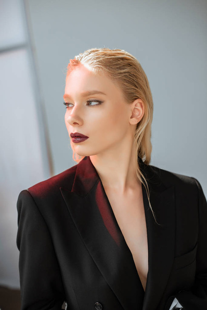 fashionable blonde young woman posing in black suit with red light on grey - Φωτογραφία, εικόνα