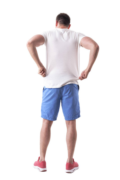 Vue arrière du jeune bel homme ajustant et revêtant des vêtements d'été. Corps entier isolé sur fond blanc
.  - Photo, image