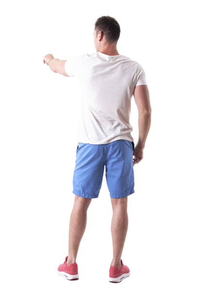 Rückansicht eines Mannes in Sommerkleidung, der mit dem Finger nach links zeigt. Ganzkörper isoliert auf weißem Hintergrund.  - Foto, Bild