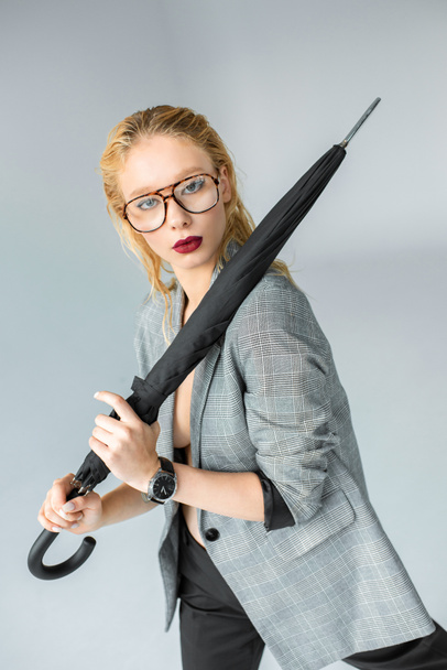 attractive blonde girl in eyeglasses posing with umbrella isolated on grey - Foto, Imagen