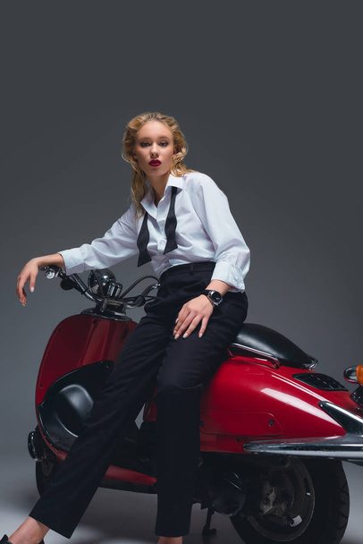 beautiful fashionable model posing on red retro scooter on grey - 写真・画像