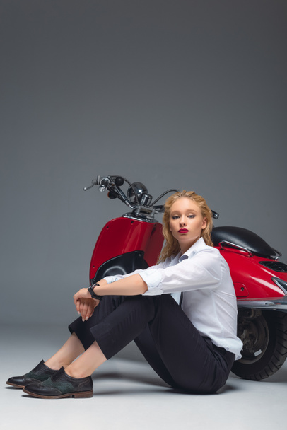 elegant fashionable girl sitting near red scooter on grey - Foto, Bild