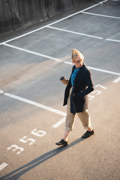 beautiful stylish girl with coffee to go walking on parking - Photo, image