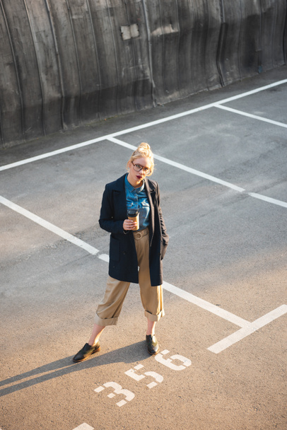 stylish young woman with coffee to go posing on parking - Foto, Imagen