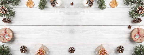 Creative frame made of Christmas tree branches on white wooden background with gift boxes, pine cones. Xmas and New Year theme. Flat lay, top view, space for text, wide composition - Photo, Image